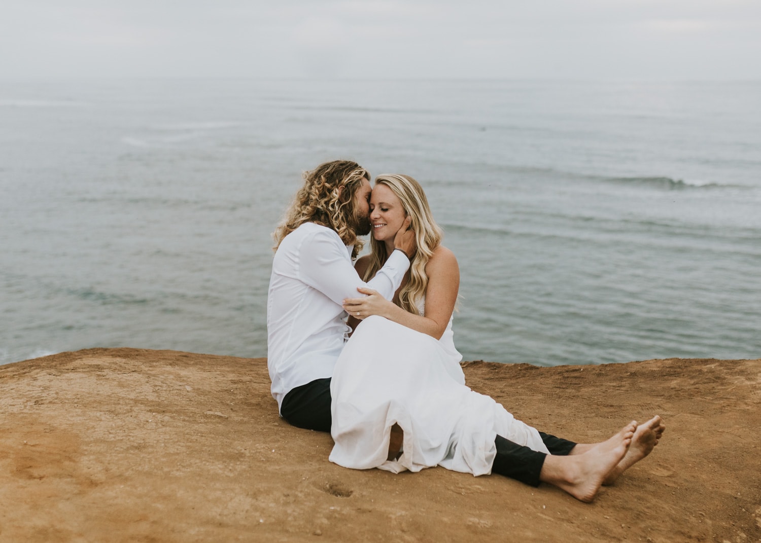 A bride and groom sitting and kissing at Sunset Cliffs Natural Park in San Diego, California during their sunrise elopement.