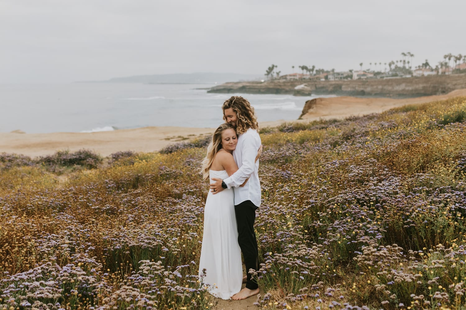A bride and groom hugging by the coast of California on their wedding day.