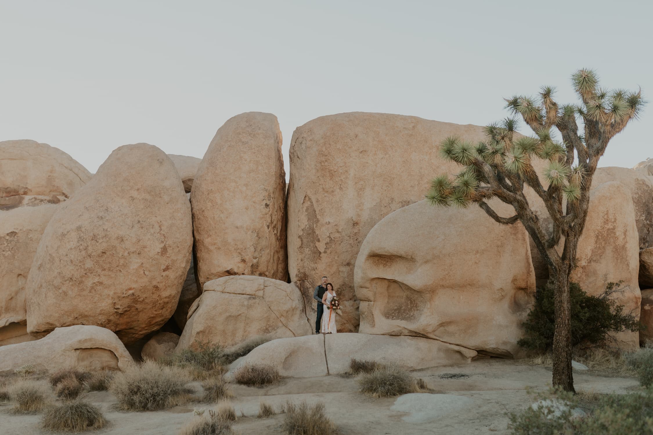 A couple standing in front of stacked boulders on their wedding day in Joshua Tree National Park.