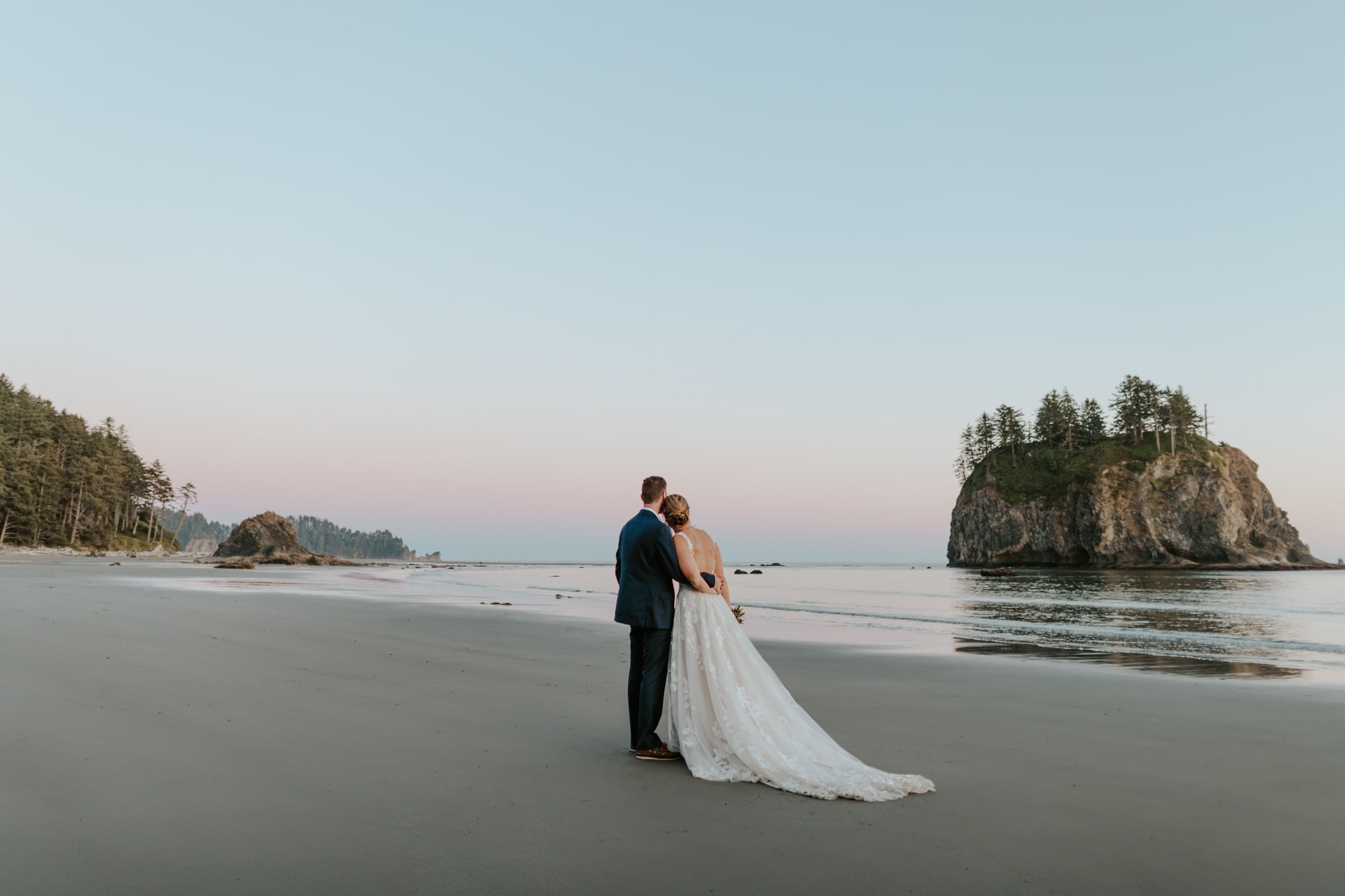 A couple in wedding attire looking at the rock formations on Second Beach in Olympic National Park.