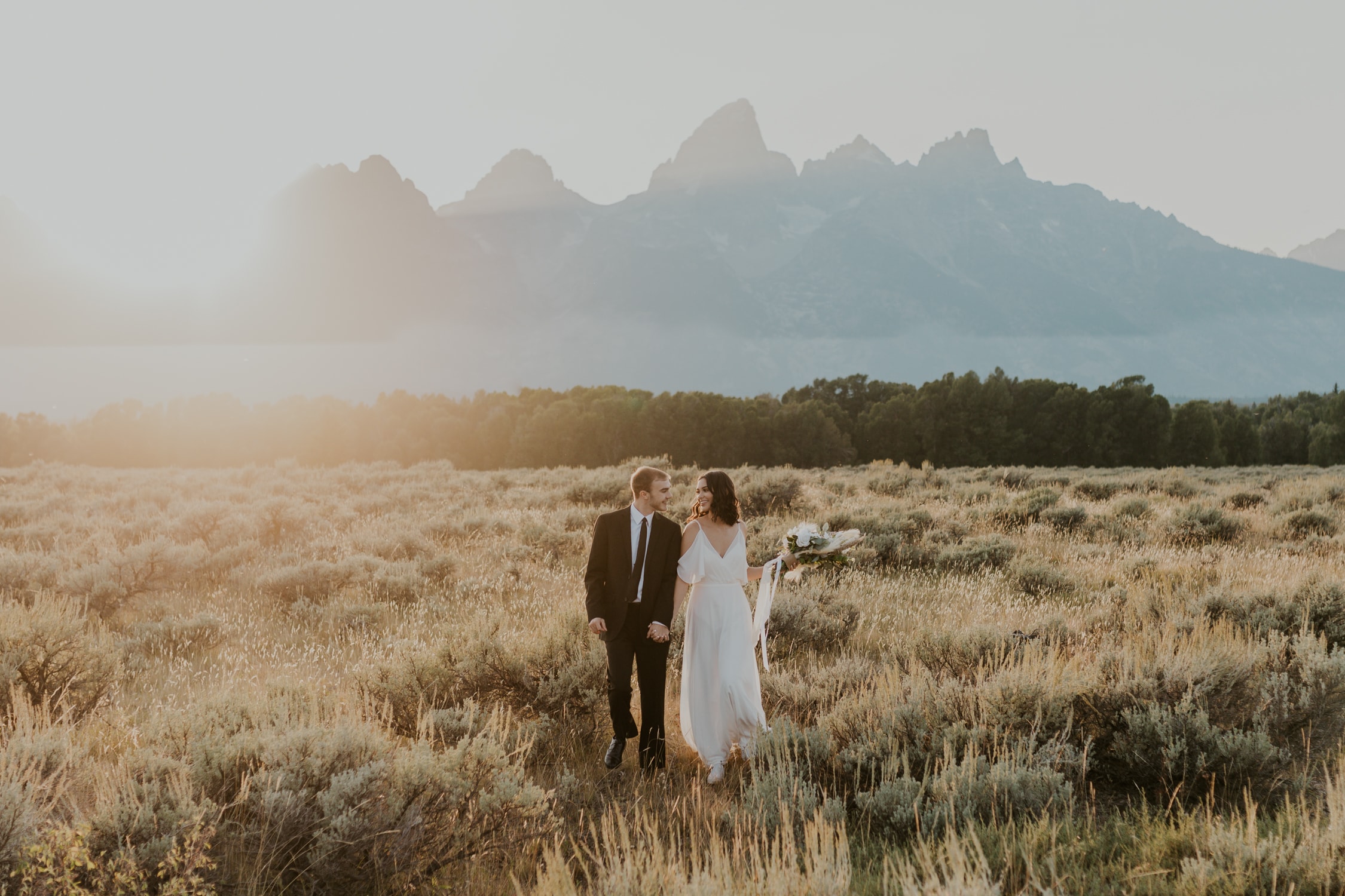 A bride and groom holding hands and walking towards the camera on their elopement day in Grand Teton National Park.