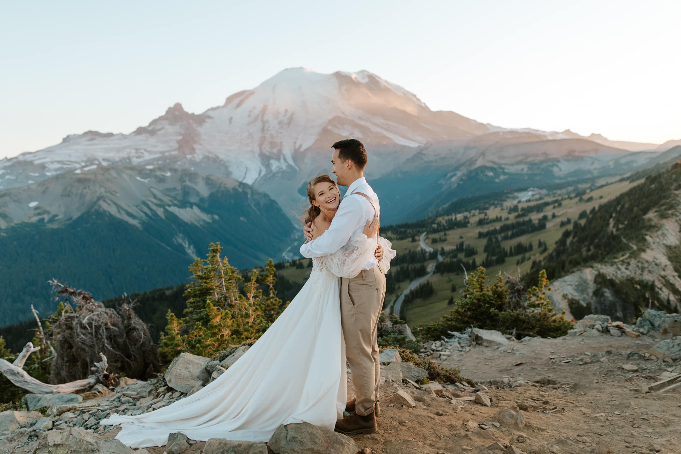 A couple in wedding attire hugging and laughing in front of Mt. Rainier.