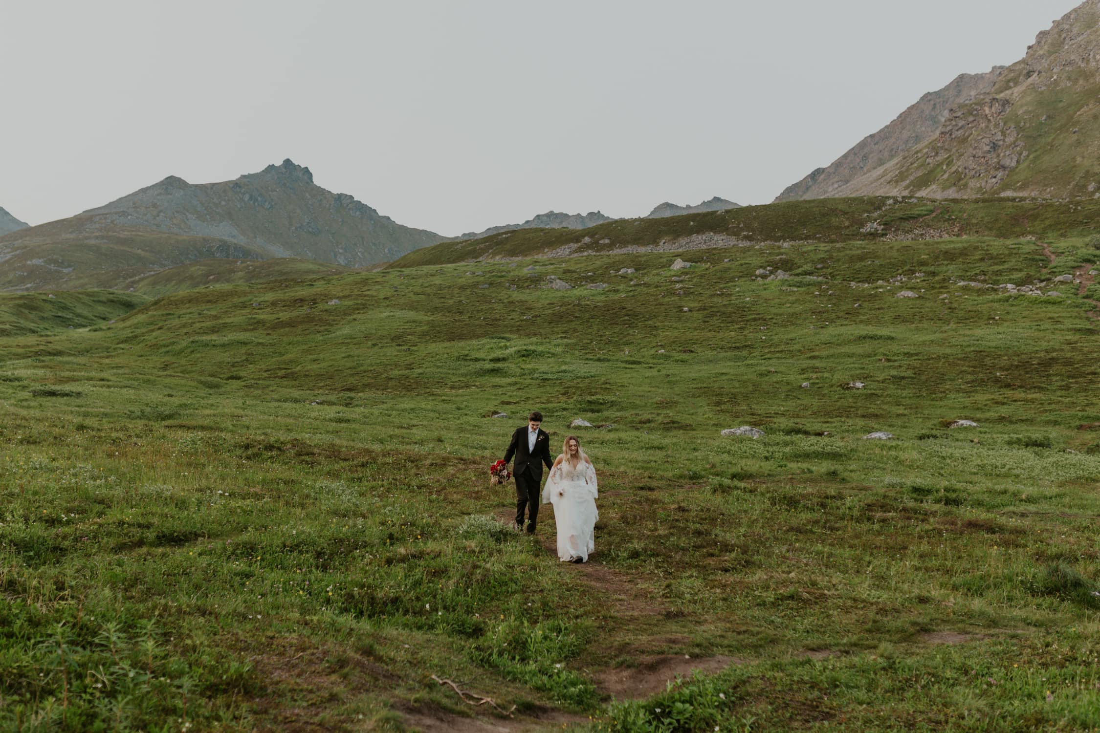 A bride and groom walking down a mountain in Alaska.