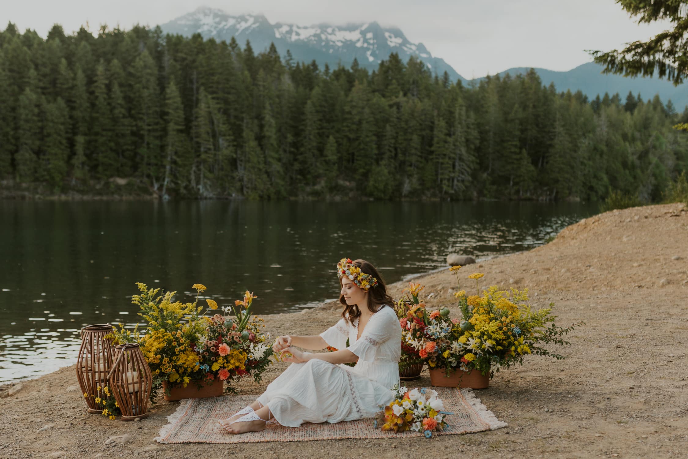 A bride playing with her wedding ring while sitting on the ground next to a lake with lots of yellow flowers in Olympic National Park.