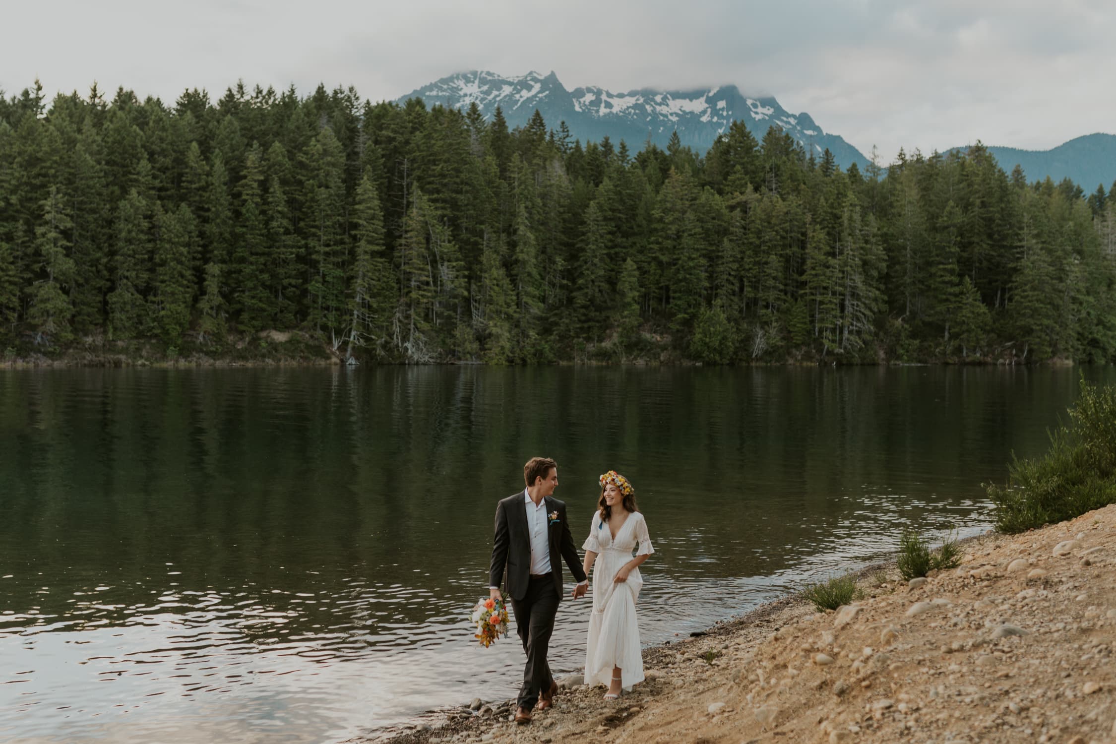 A bride and groom holding hands and walking along the shore of a lake in Washington State.