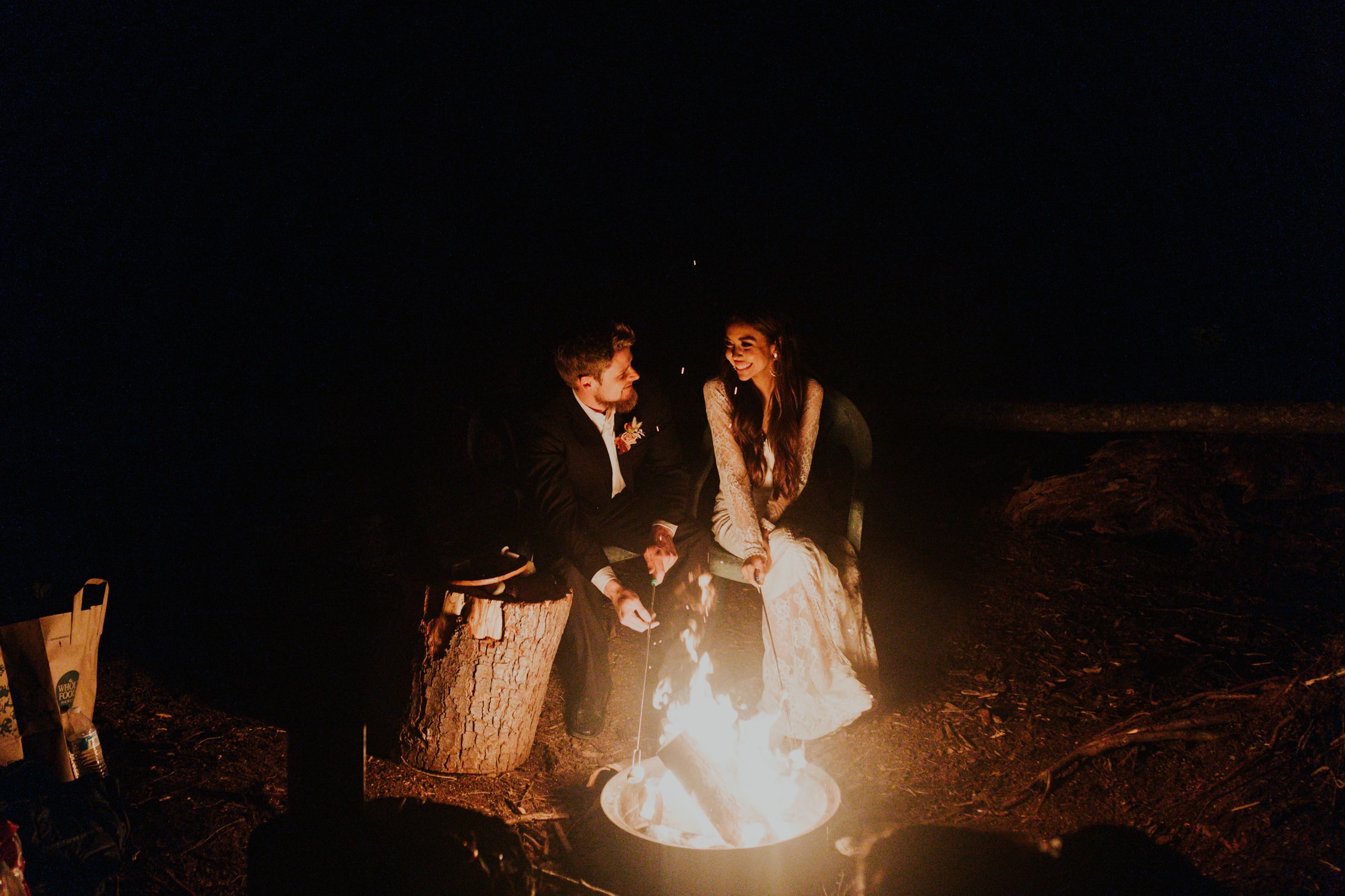 A bride and groom roasting marshmallows on a fire on their elopement day.