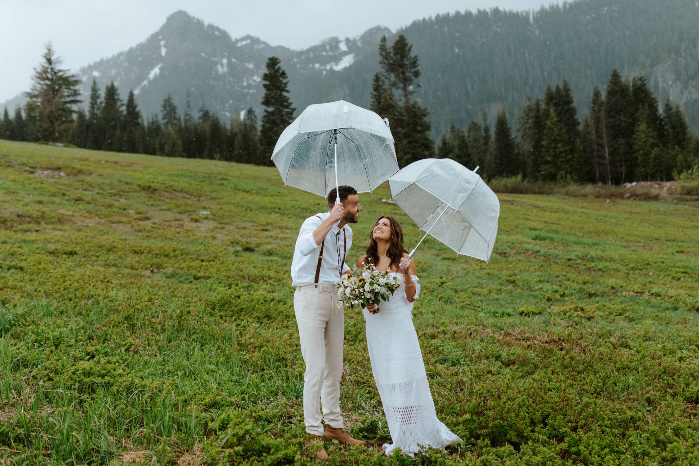 A bride and groom holding umbrellas and looking up at the sky smiling in Washington.