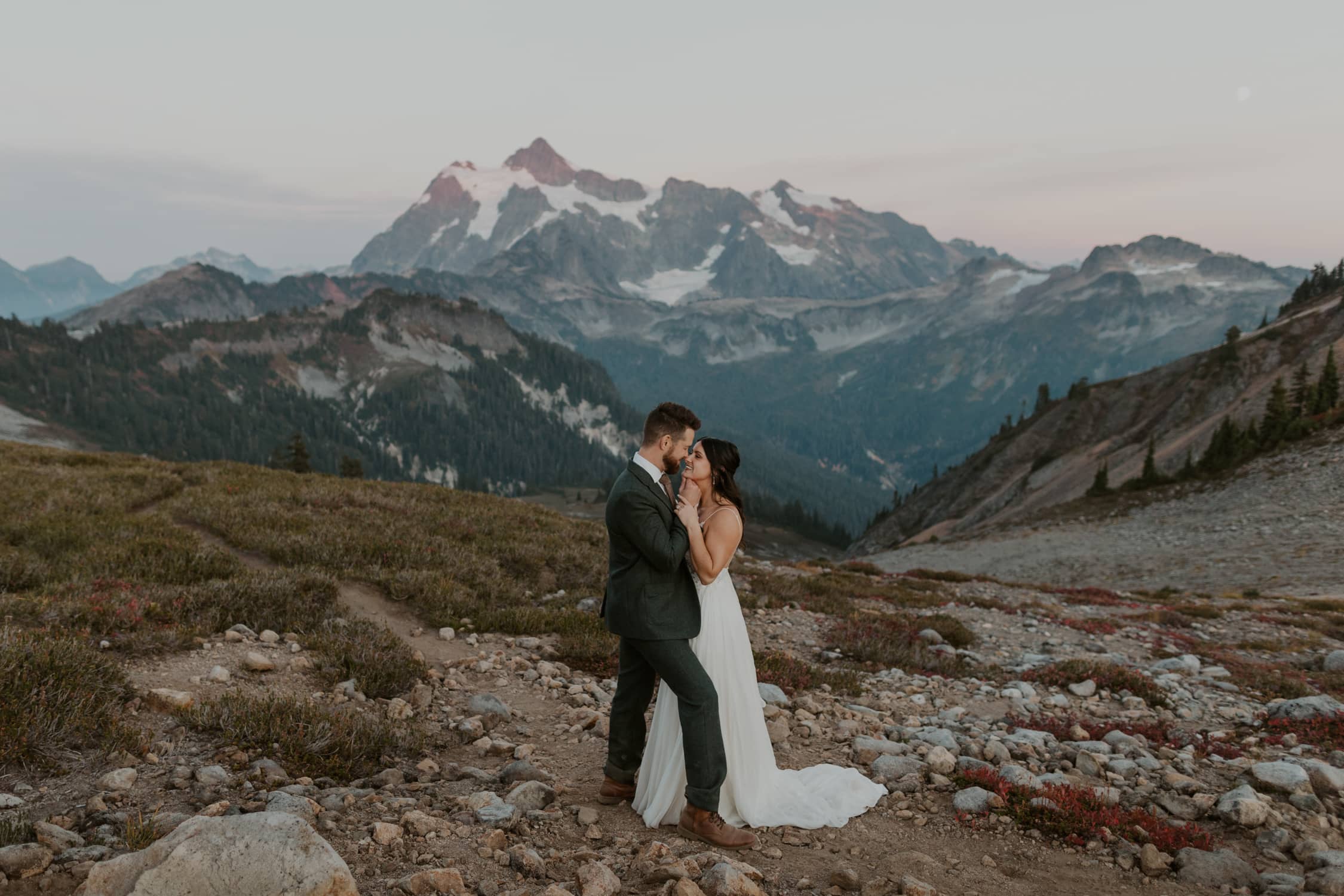A bride and groom facing each other with their eyes closed in front of a mountain in North Cascades National Park.