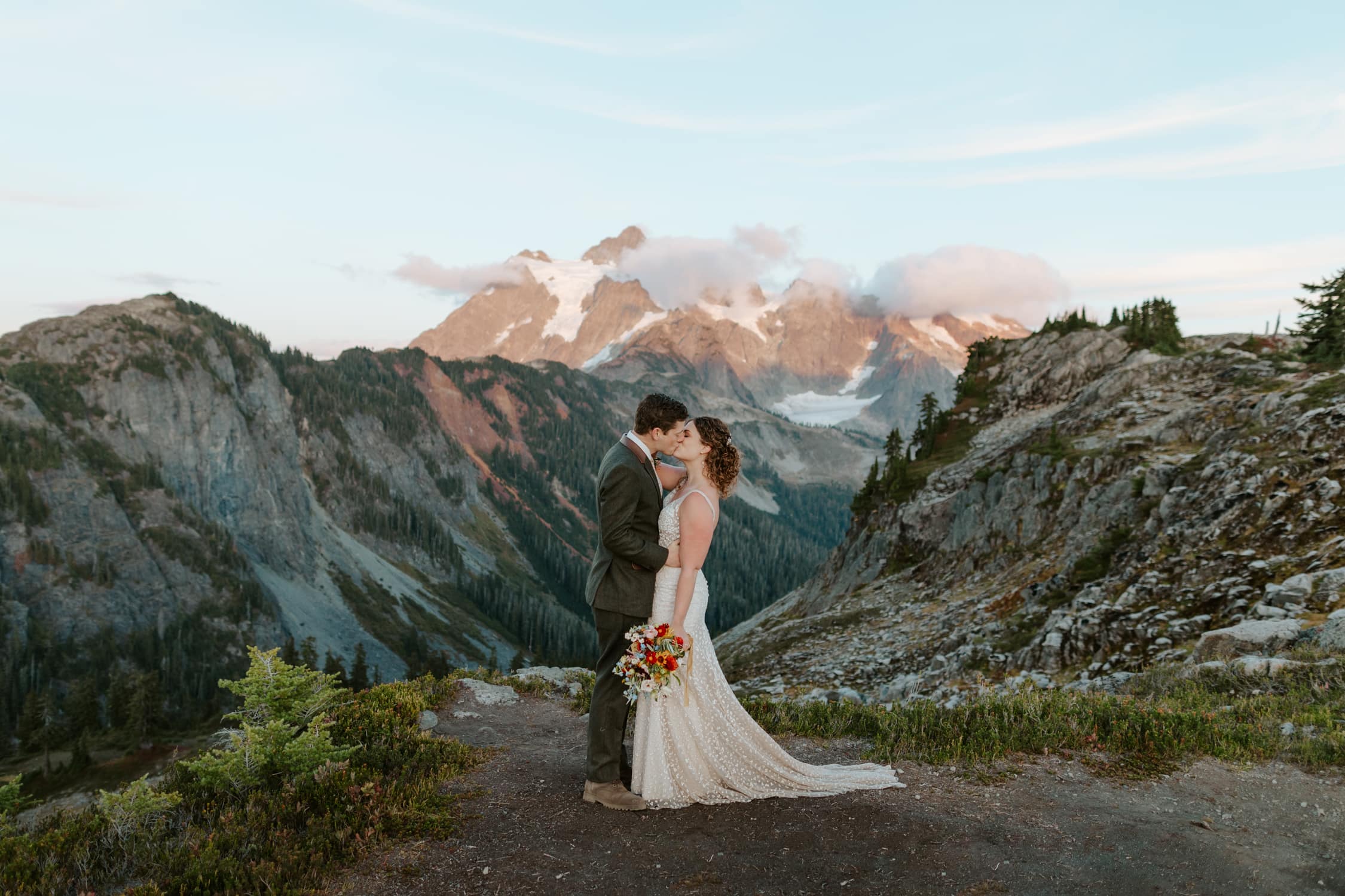 A couple in wedding attire kissing in front of Mt. Shuskan.