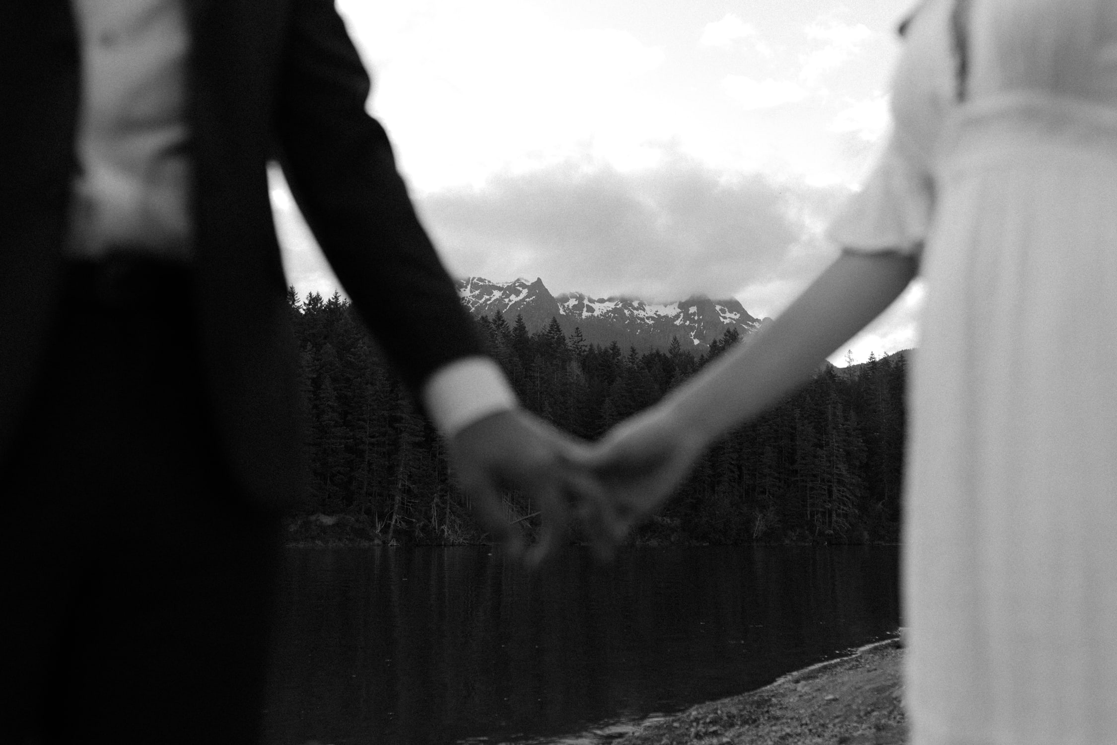 A bride and groom holding hands in front of Lake Cushman.