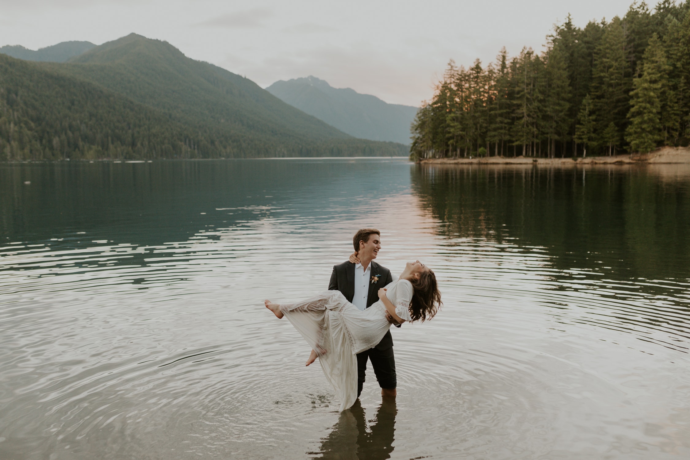A bride and groom laughing in Lake Cushman on their wedding day.