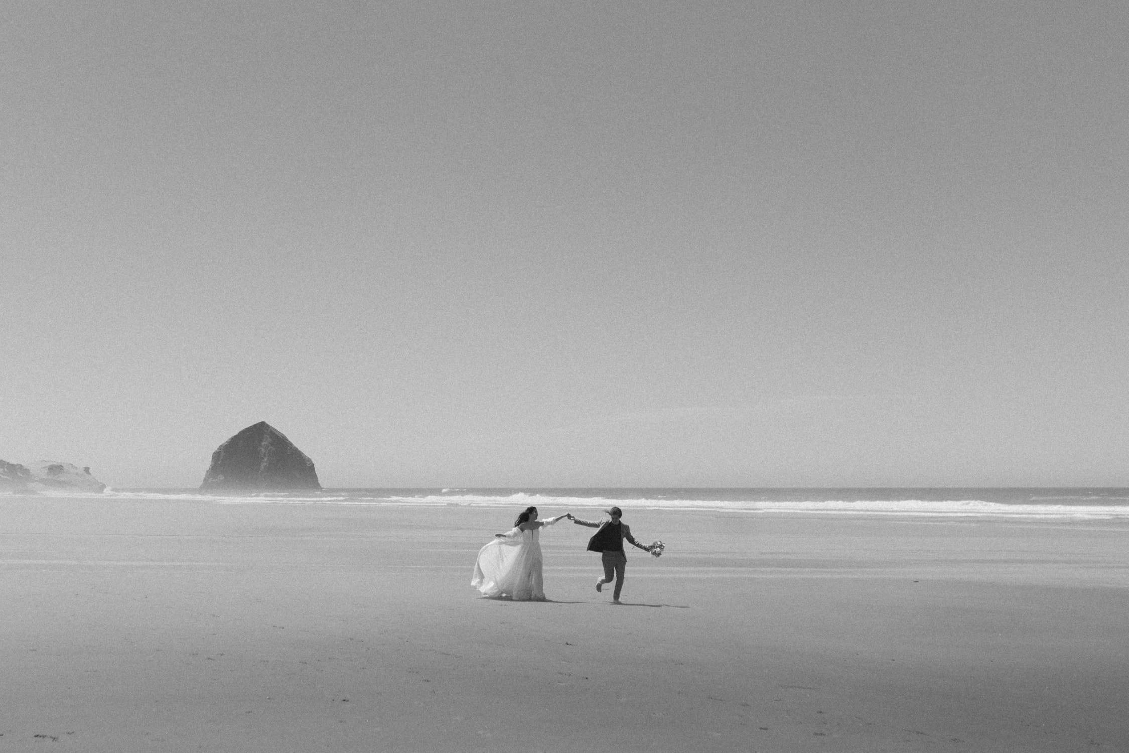 A bride and groom holding hands and running towards the camera on Cannon Beach.
