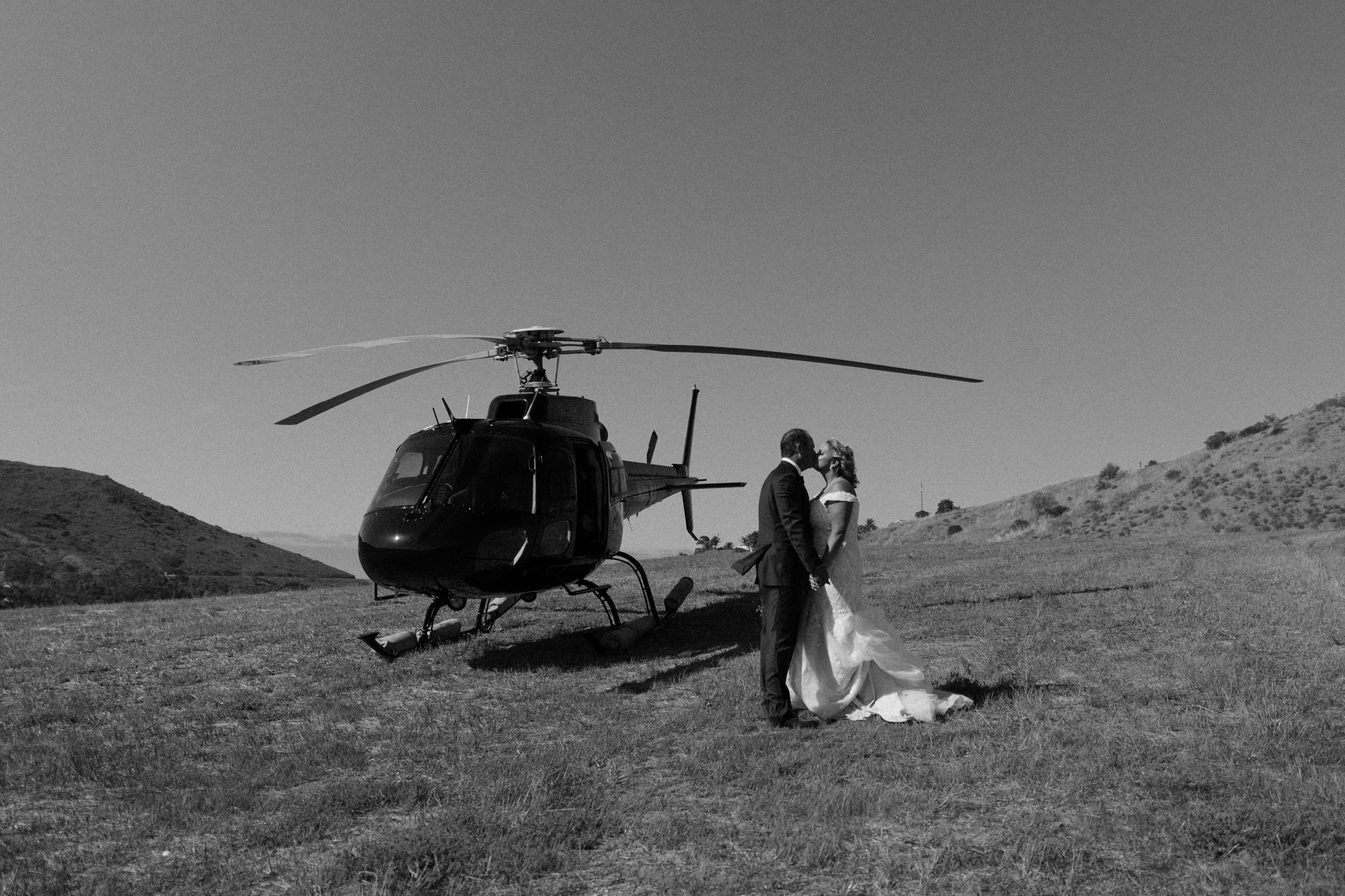 A bride and groom kissing next to a helicopter.