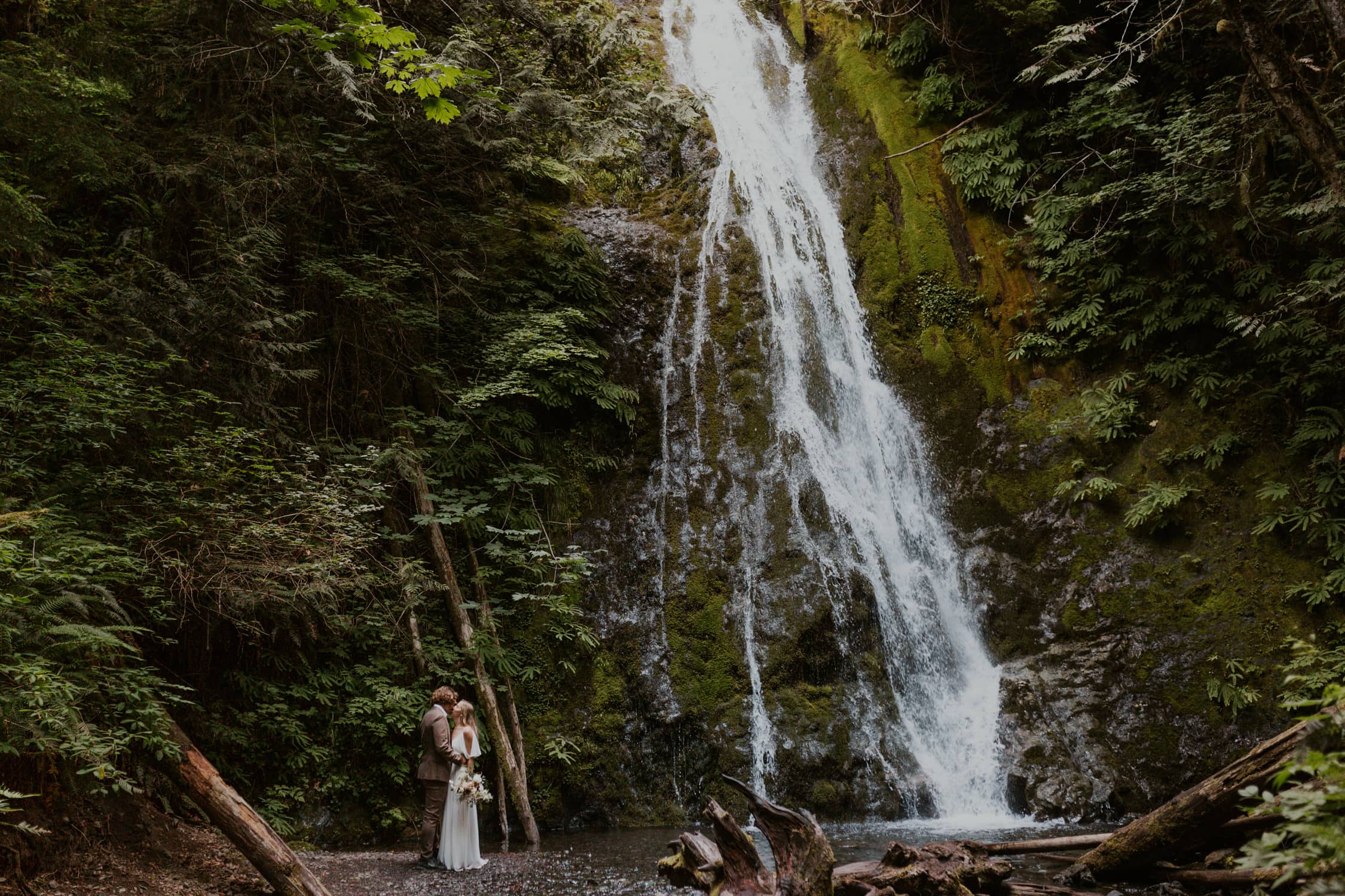 A bride and groom kissing next to Madison Falls, located in Olympic National Park in Washington State.