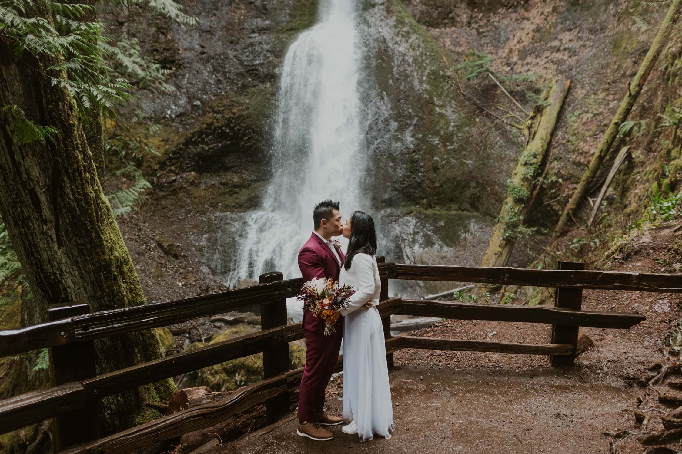 A bride and groom kissing in front of Marymere Falls.