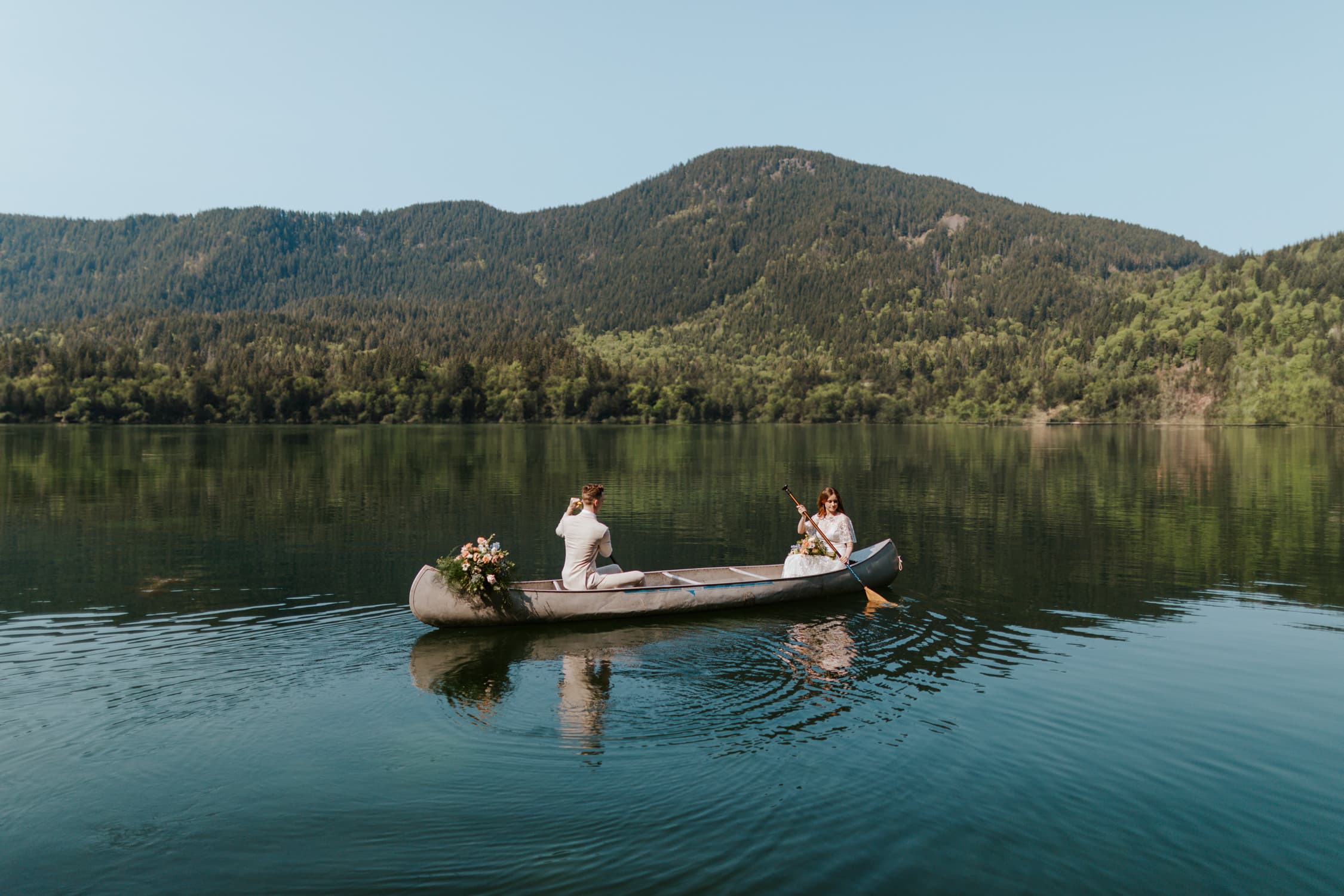 A couple in wedding attire canoeing on Lake Sutherland in Olympic National Park on their wedding day.