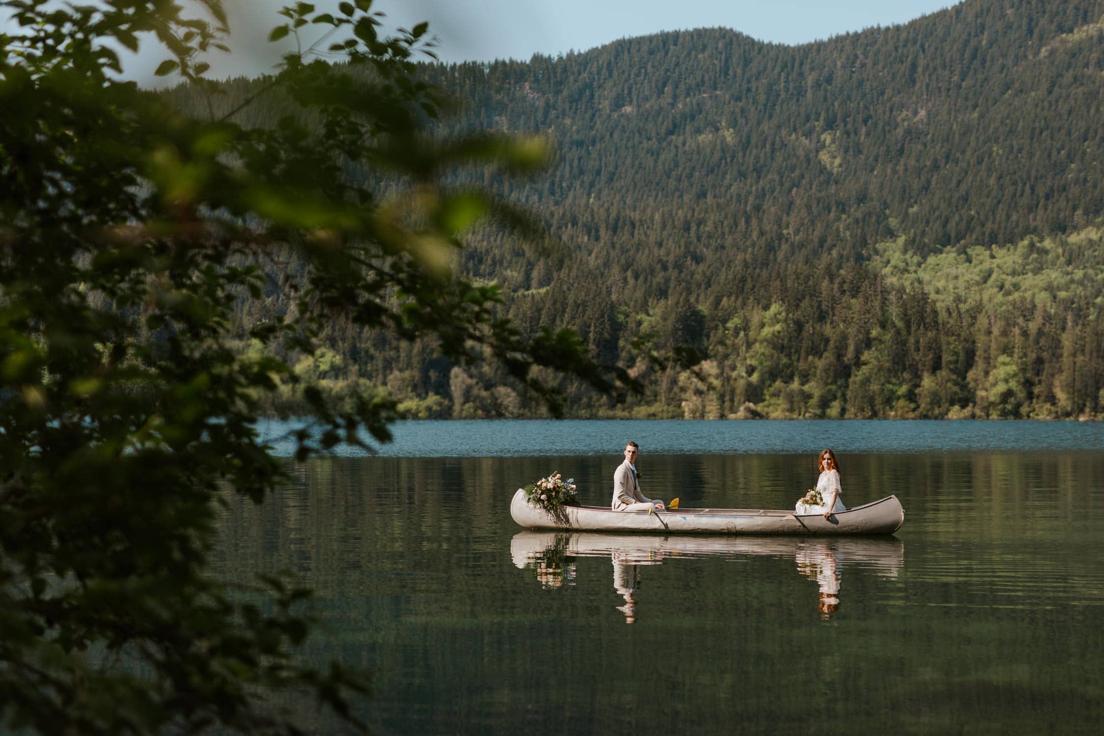 A couple in wedding attire canoeing on Lake Sutherland in Olympic National Park on their wedding day.