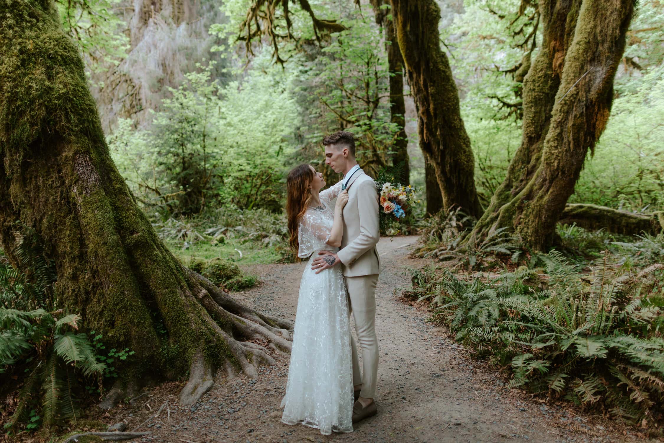 A bride and groom looking up at each other in the Hoh Rainforest on their elopement day.