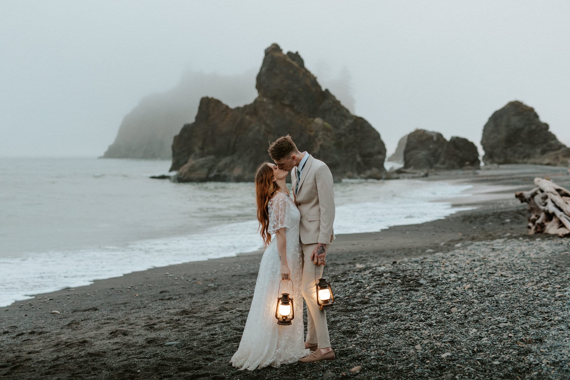 A bride and groom holding lanterns and kissing on Ruby Beach in Olympic National Park.