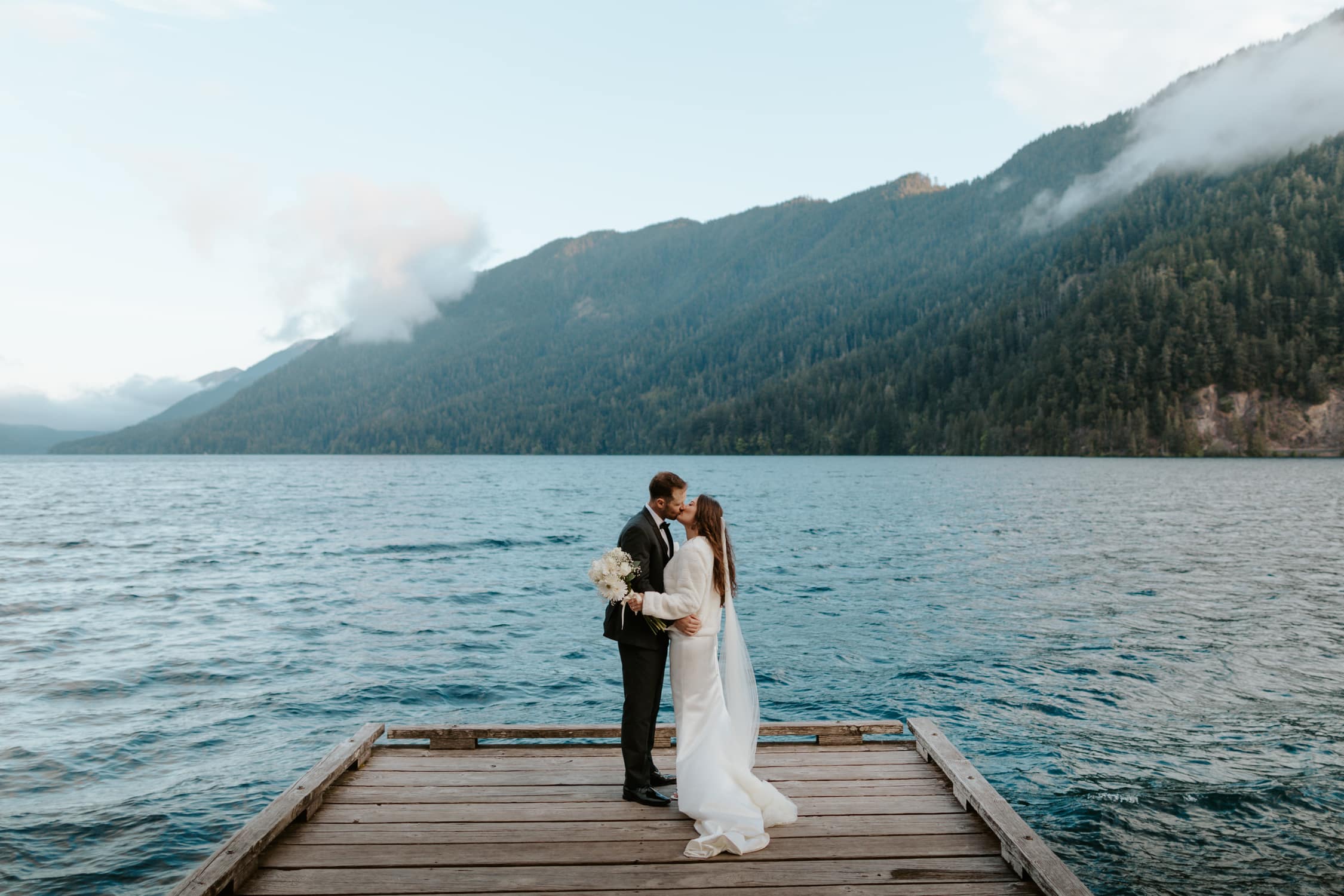 A bride and groom kissing on a dock on Lake Crescent in Olympic National Park.