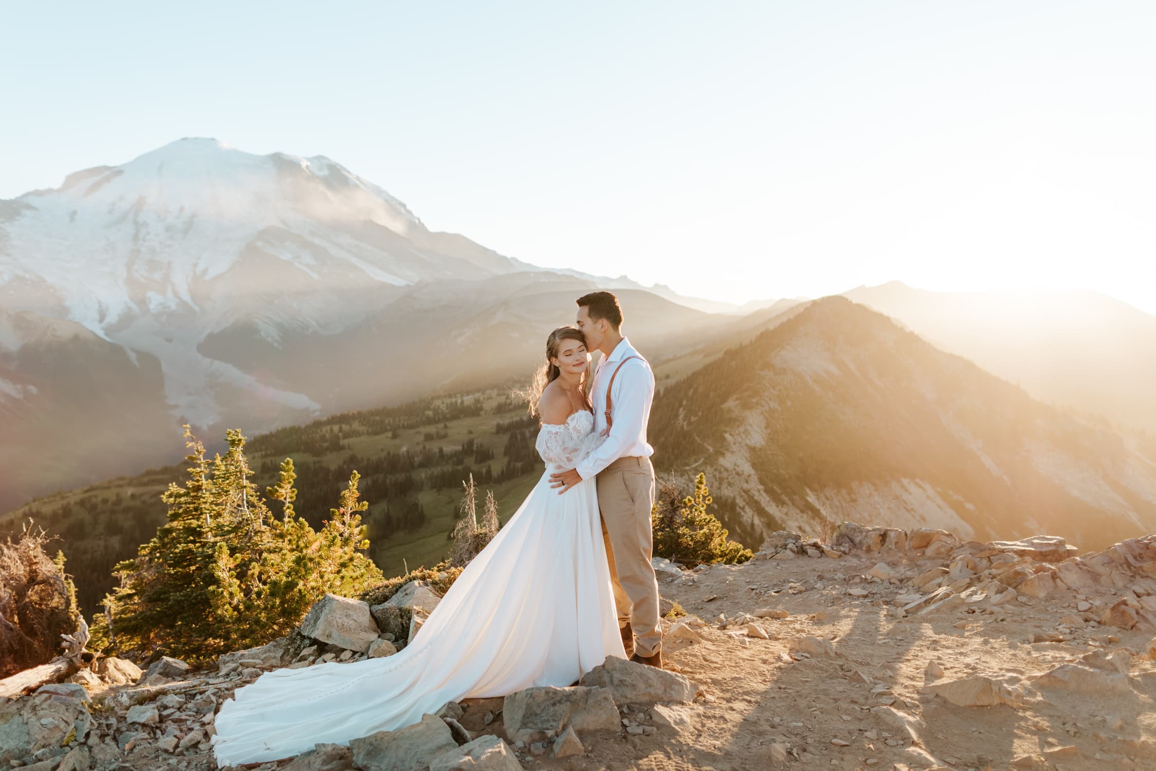 A groom kissing his bride's head in front of Mt. Rainier in Washington.