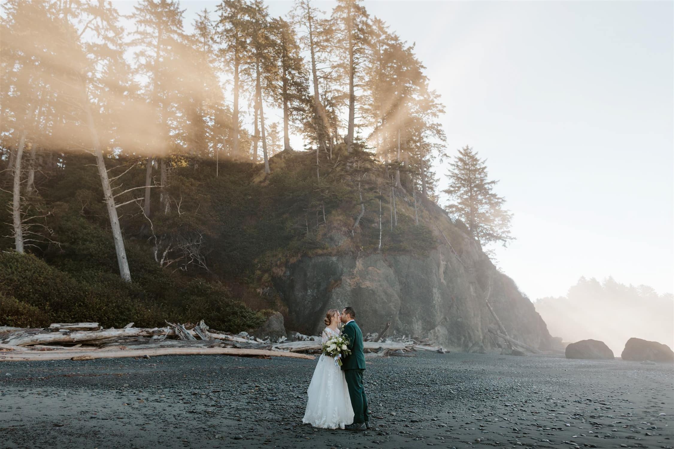 A bride and groom kissing on Ruby Beach with sun rays in the back.