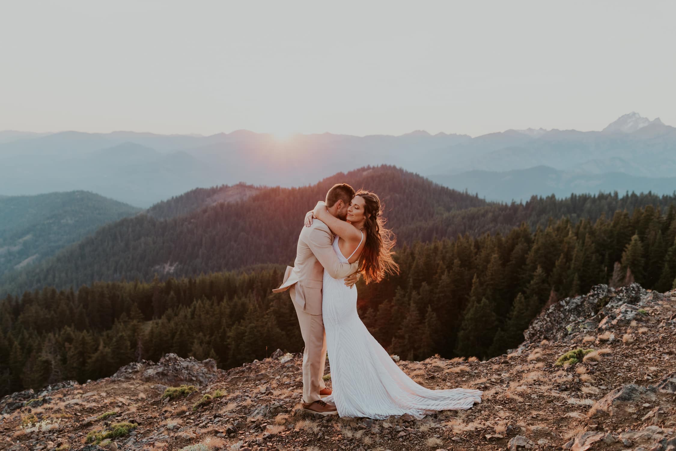 A bride and groom hugging each other on top of a mountain in Washington during golden hour.